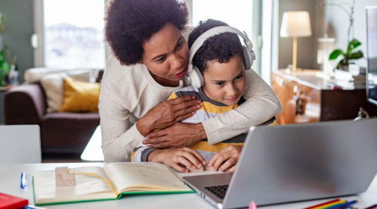 Mother hugging her son while he is listening online classes and studying