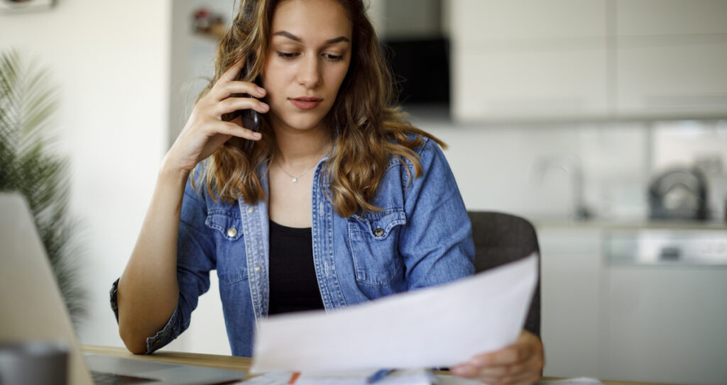 This image depicts a woman reading what appears to be a bill while on the phone.