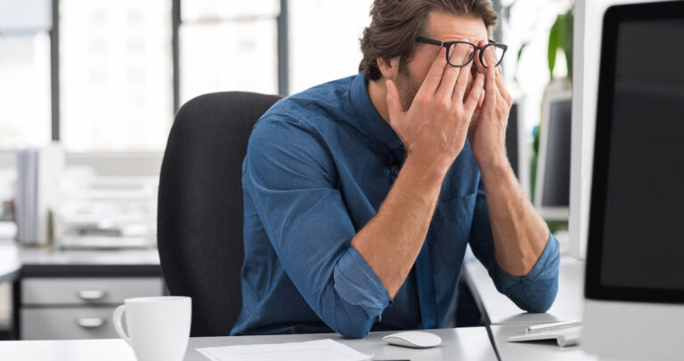 A business man in his office rubs his face to demonstrate stress.