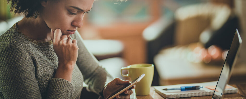 Young black woman reading a problematic text message on her mobile phone while working at home.