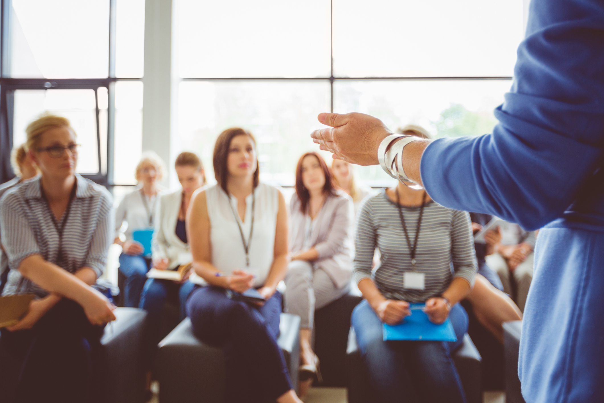 Hand of a trainer addressing group of females sitting in a conference hall. Female hand against defocused group of women attending seminar.