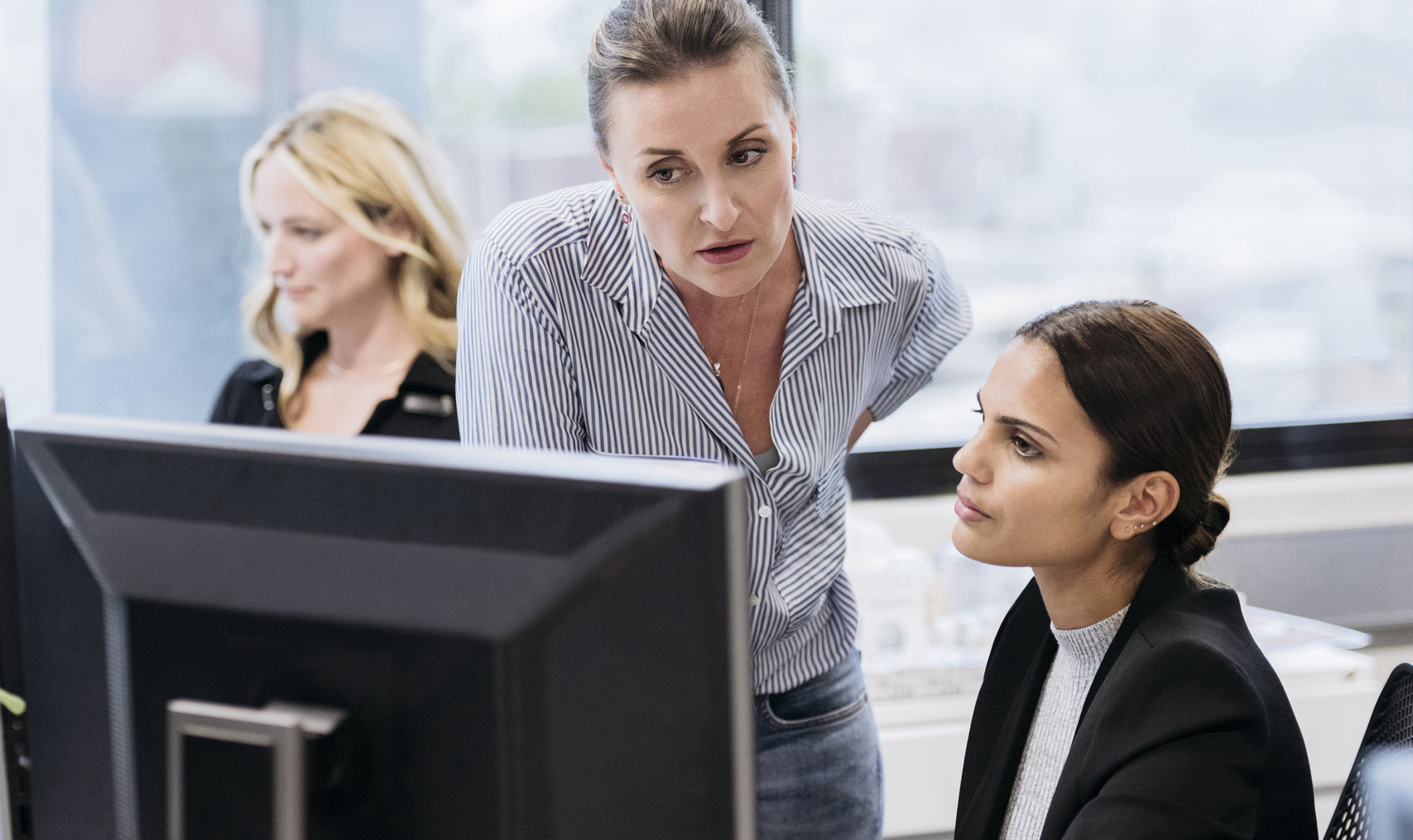 Co-workers discussing an issue at an office computer. Co-workers discussing an issue at an office computer.