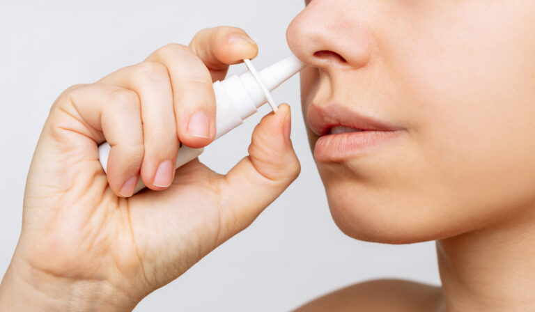 Cropped shot of a young caucasian woman using nasal spray for a runny nose and congestion isolated on a white background. Treatment of the disease. Rhinitis, sinusitis. Dependence on drops