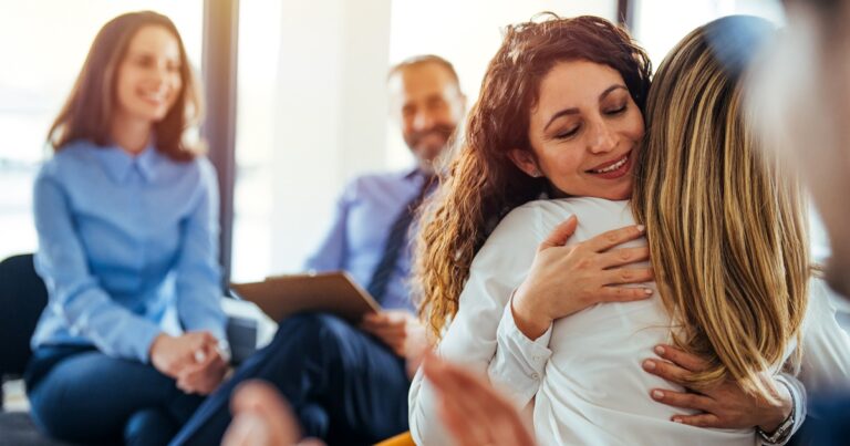 The two women are attending a group therapy session. They are showing support and kindness. Portrait of female psychologist embracing young woman during therapy session in support group