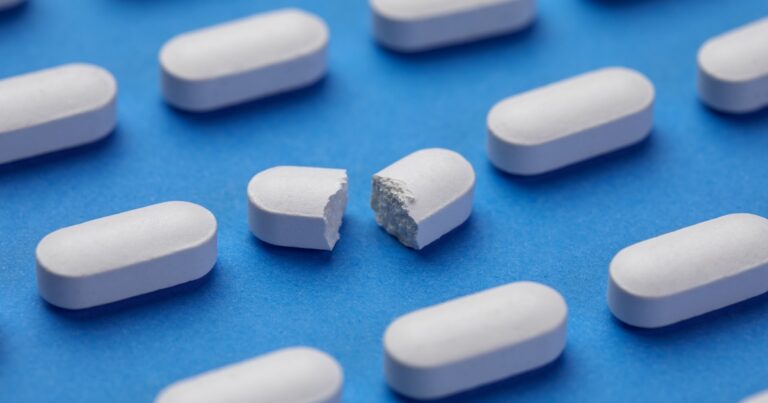 Row of White pills on blue background. One tablet is broken in half.