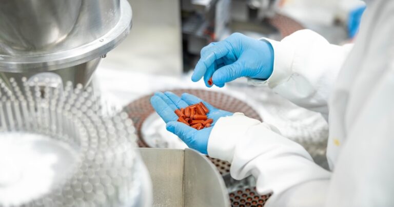 A close view of red capsules held for inspection before production, focusing on the emphasis of health safety in pharmaceuticals.