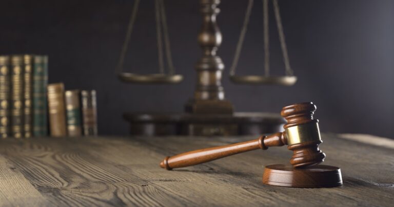 Judge's gavel and scale of justice on wooden desk. Gray background with legal books.