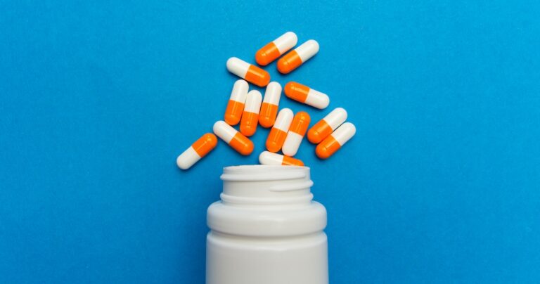 Orange white capsules (pills) were poured from a white bottle on a blue background. Medical background, template.