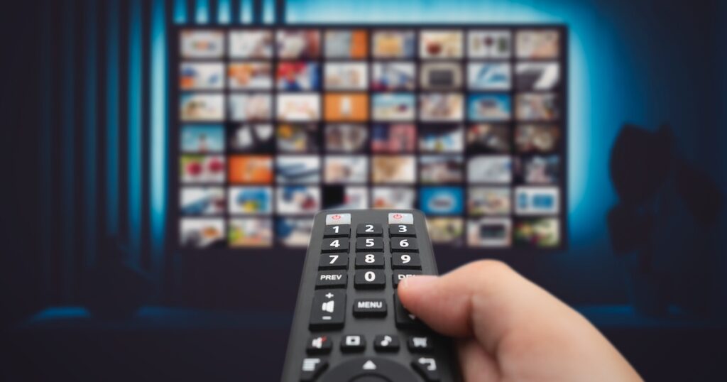 VOD service screen. Man watching TV with remote control in hand.