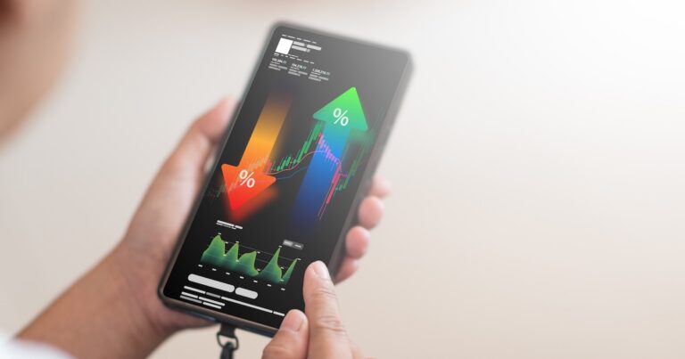 A close-up shot shows a person's hand holding a smartphone, displaying a complex financial analysis interface with upward and downward trending percentage arrows, stock market charts, and various data points. This image is perfect for illustrating concepts like investment, trading, financial growth, economic analysis, and mobile financial management.