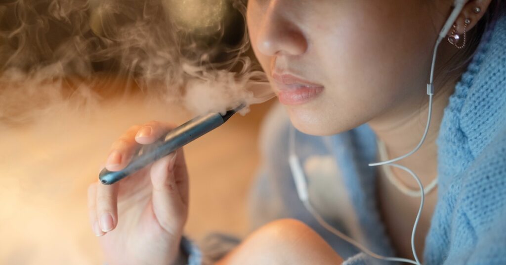 Young woman vaping an electronic cigarette for relax while working at night