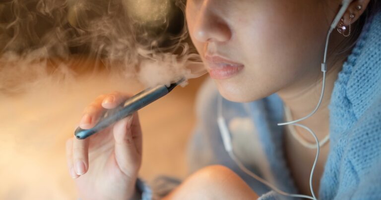Young woman vaping an electronic cigarette for relax while working at night