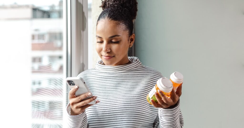 A young woman standing by the window and researching about the medicine online