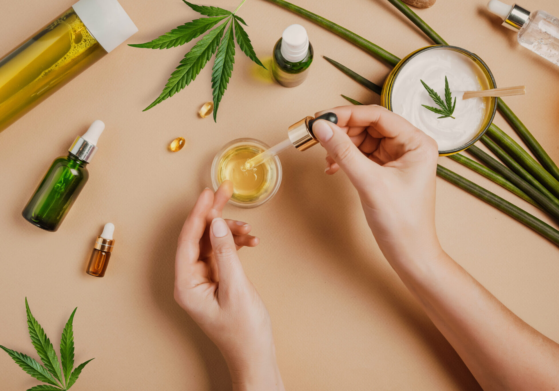 Pipette with CBD cosmetic oil in female hands on a table background with cosmetics, cream with cannabis and hemp leaves, marijuana Pipette with CBD cosmetic oil in female hands on a table background with cosmetics, cream with cannabis and hemp leaves, marijuana. Flat lay, top view.