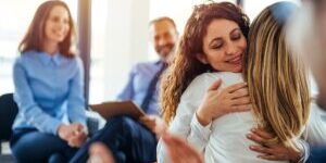 The two women are attending a group therapy session. They are showing support and kindness. Portrait of female psychologist embracing young woman during therapy session in support group