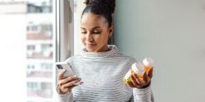 A young woman standing by the window and researching about the medicine online