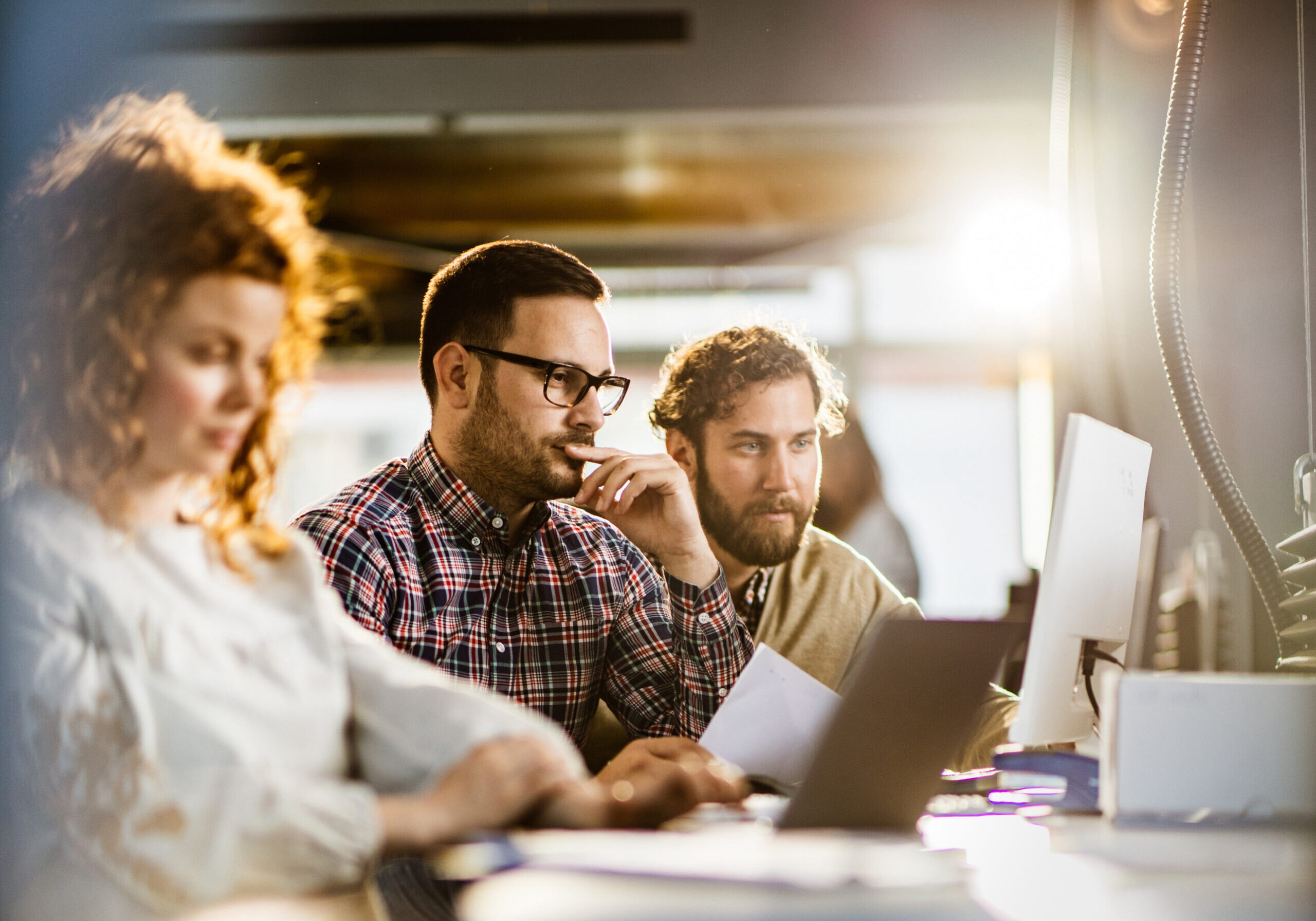 Group of colleagues working at corporate office. Focus is on pensive man with glasses working on PC with his colleague. Copy space.