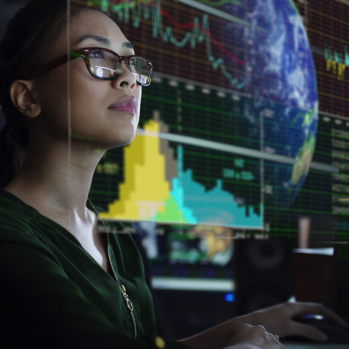 See through screen Photo of a young Asian woman looking at see through global & environmental data whilst seated in a dark office. The data is projected on a see through (see-thru) display.