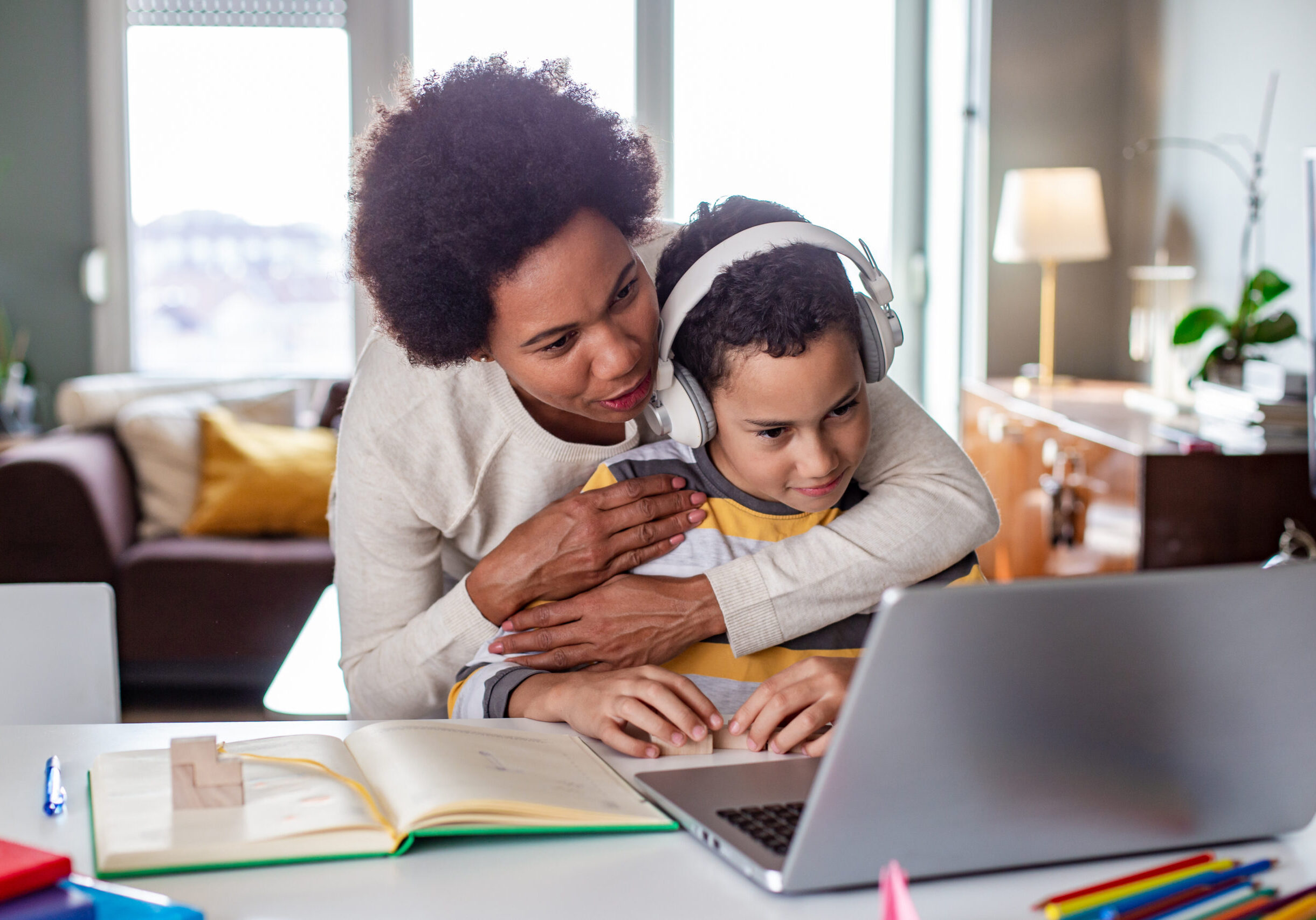 Mother hugging her son while he is listening online classes and studying