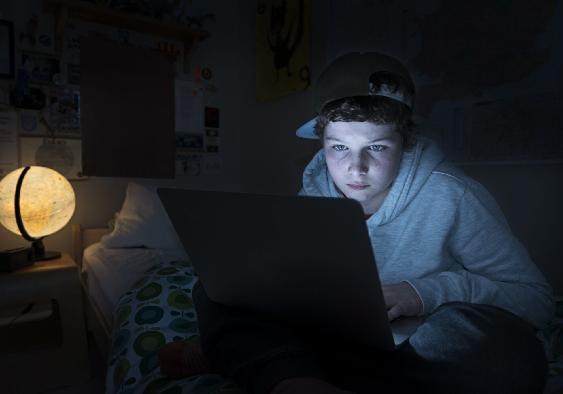 Online Young Teen in His Bedroom Portrait of a young teenage boy online in his bedroom. He is lying on his bed in a darkened room and he is illuminated by the light coming from the screen from his laptop as he surfs the web late at night.