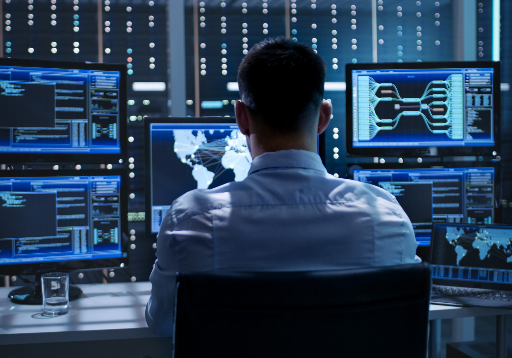 System Security Specialist Working at System Control Center. Room is Full of Screens Displaying Various Information. System Security Specialist Working at System Control Center. Room is Full of Screens Displaying Various Information.
