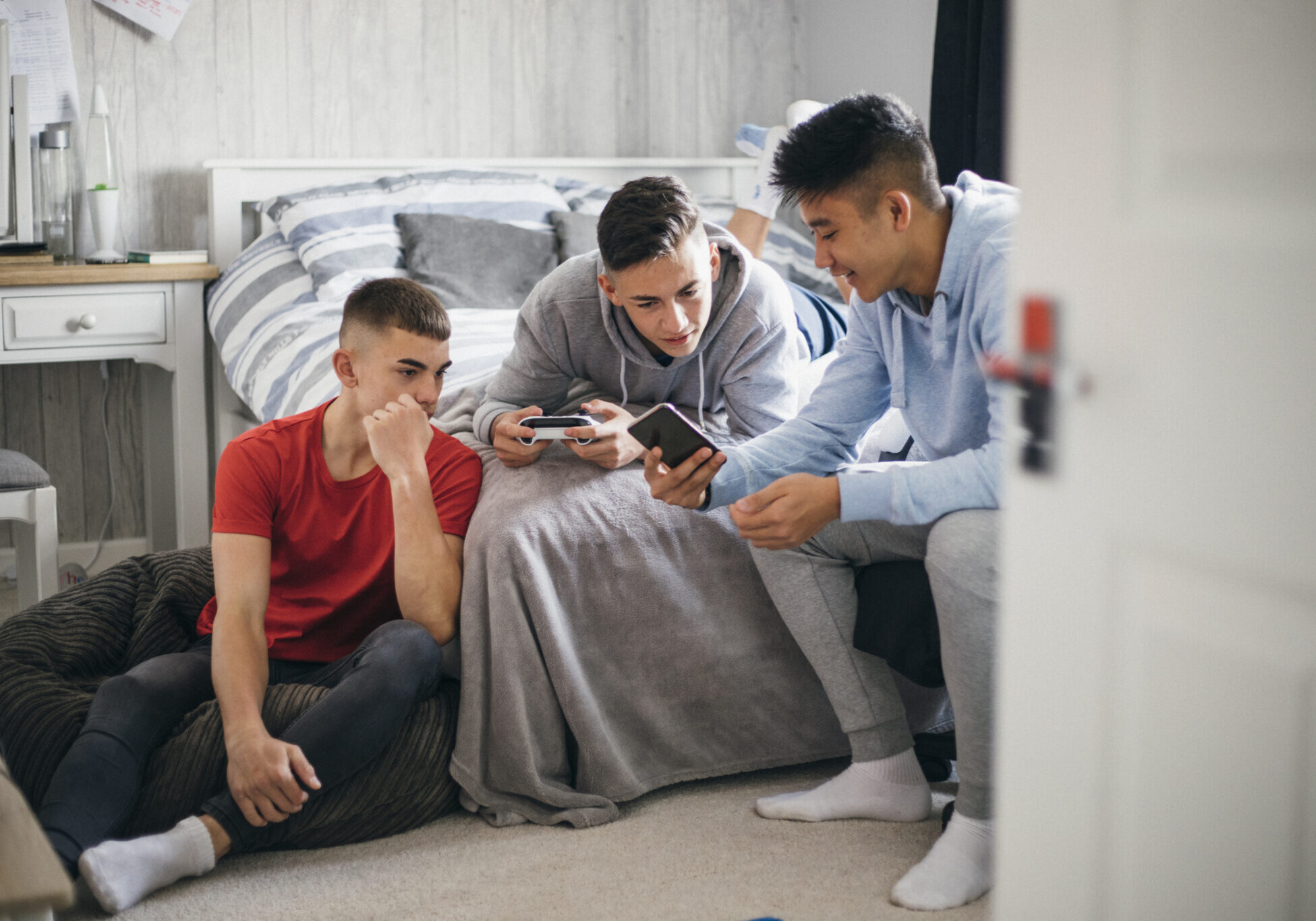 Three teenage boys relaxing and having fun while playing on a games console in a bedroom.