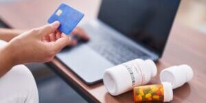 Young blonde woman using laptop and credit card buying pills at home